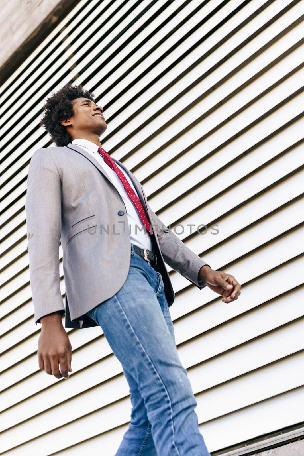 Black Businessman wearing suit walking in urban background. by javiindy