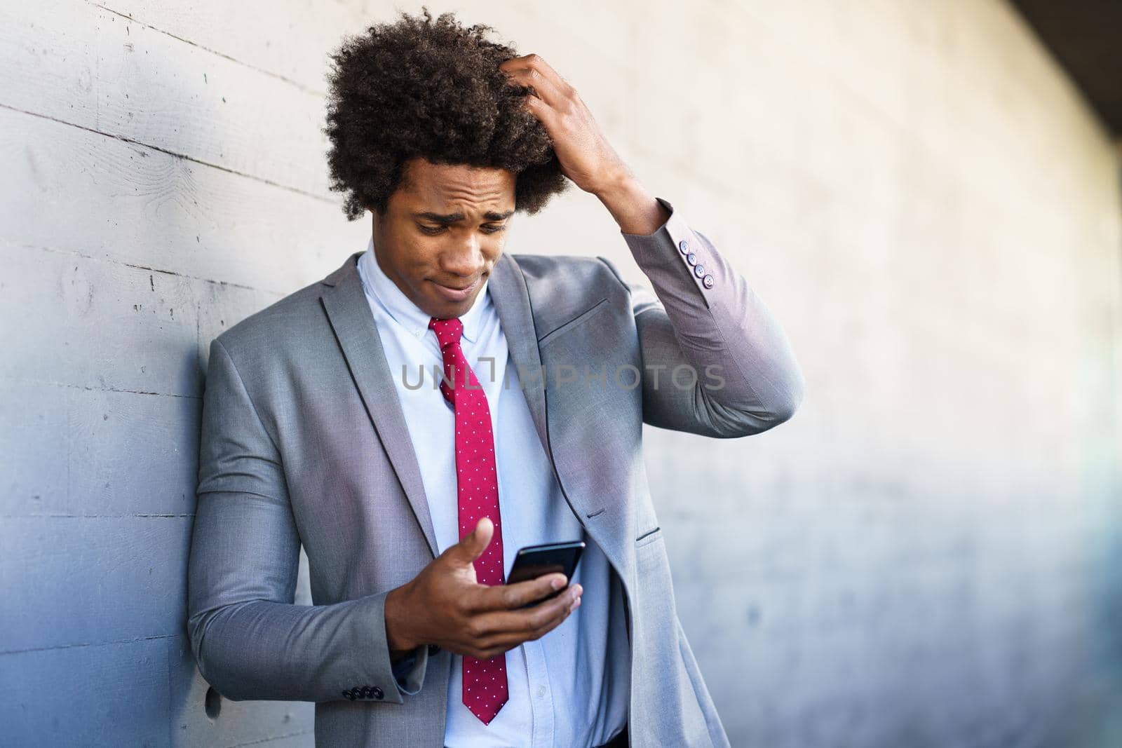 Worried Black Businessman using his smartphone near an office building. Man with afro hair.