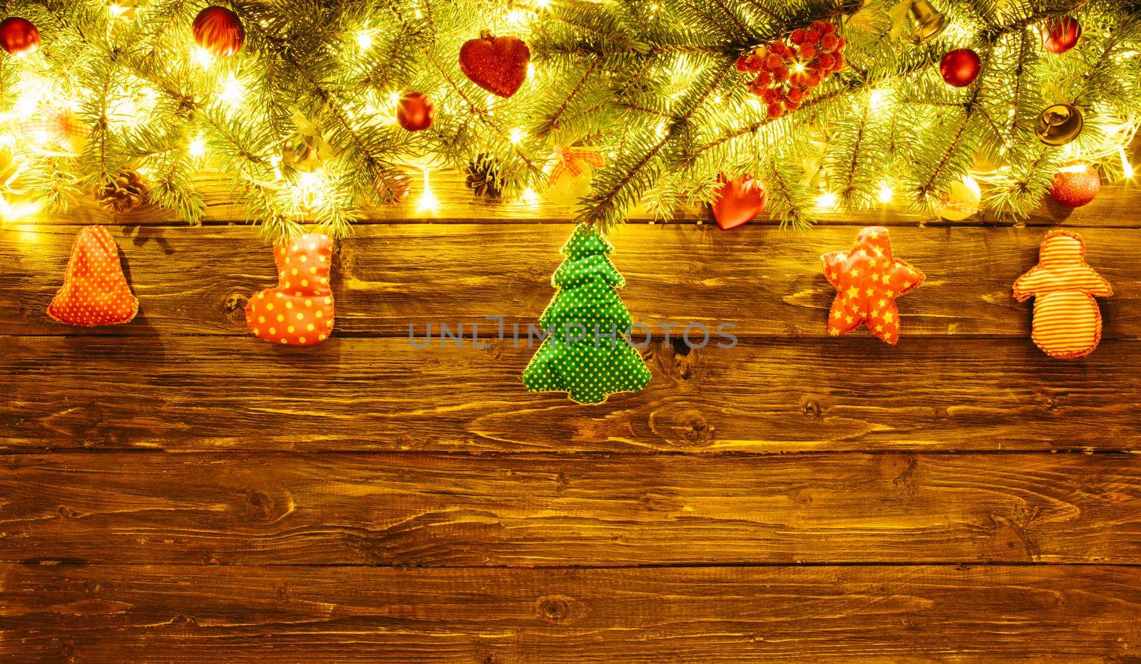 Blurred Christmas background, with fir branches, fairy lights and christmas decorations on brown wooden plank .