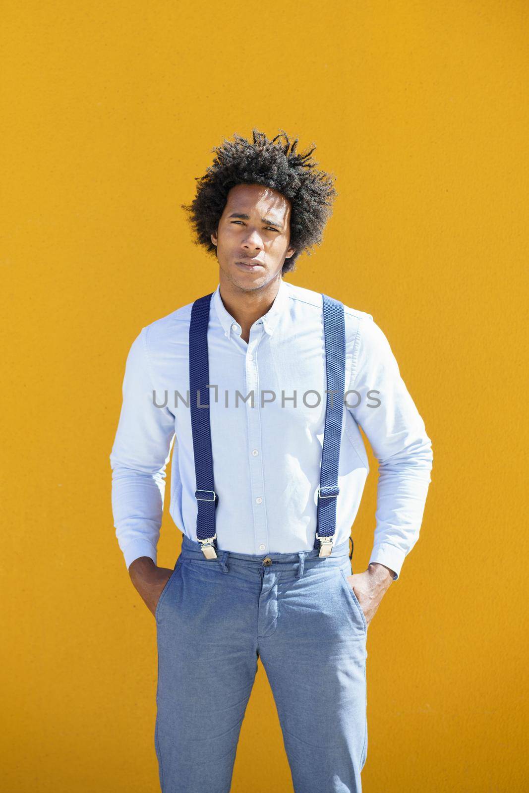 Black man with afro hair on yellow urban background wearing shirt and suspenders. by javiindy