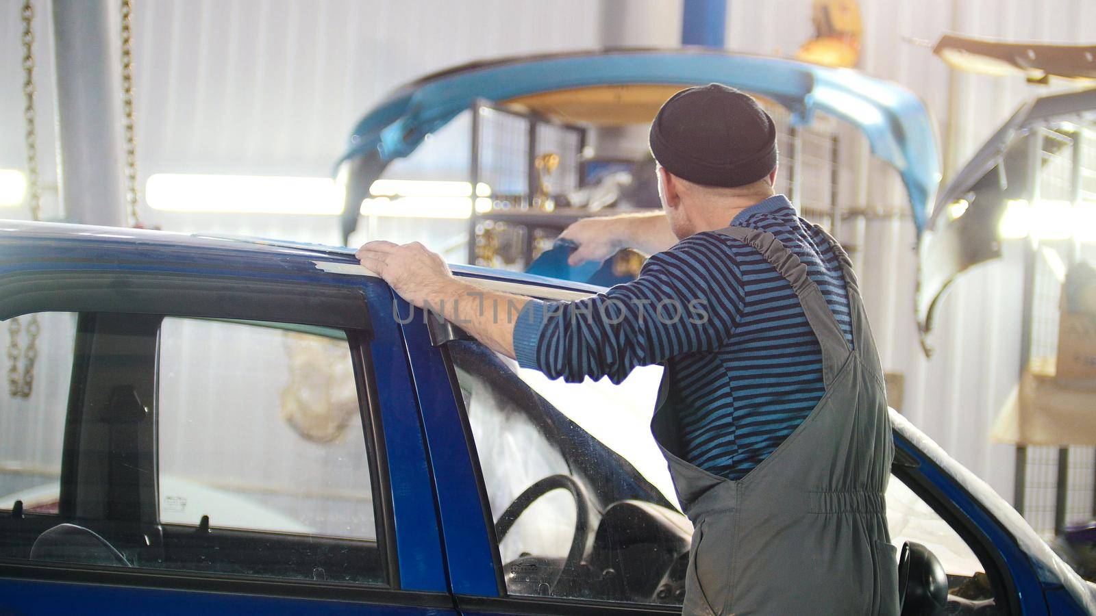 Professional car service - a worker polishes a blue automobile, telephoto