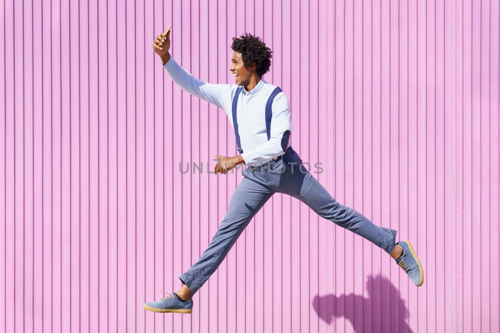 Black man taking a selfie with his smartphone while jumping outdoors. by javiindy