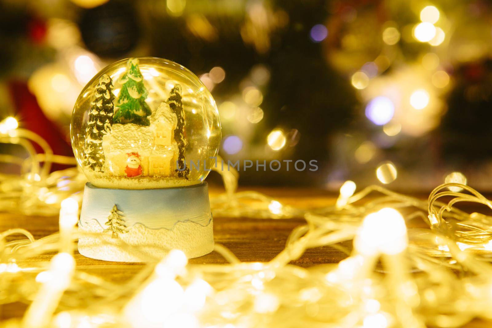 Christmas snow globe on wooden table over christmas lights .