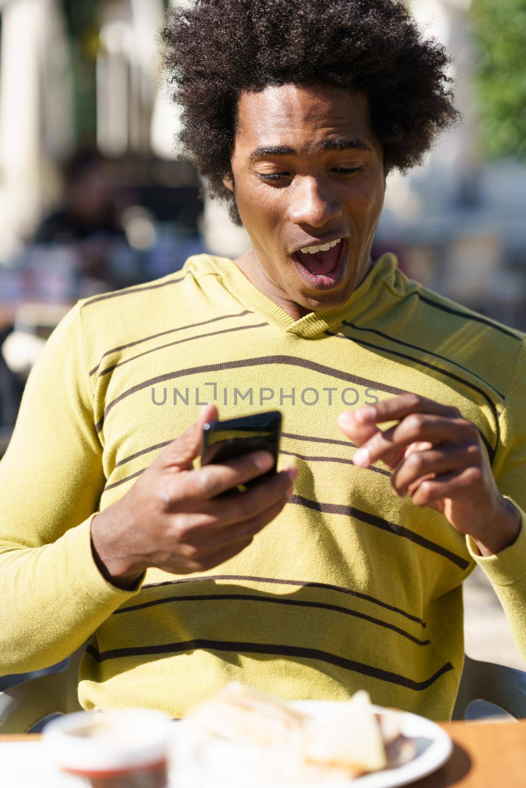 Cuban Black taking a photo with his smartphone to a snack in a bar sitting at the table outdoors on his trip to Granada, Spain.