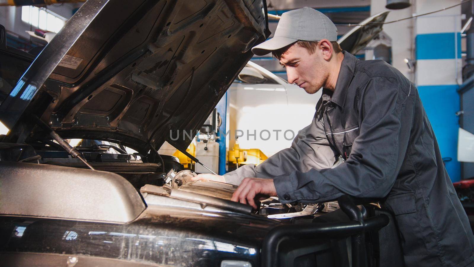 Mechanic male in automobile garage processing engine diagnostic - checking in hood of the car for luxury SUV by Studia72