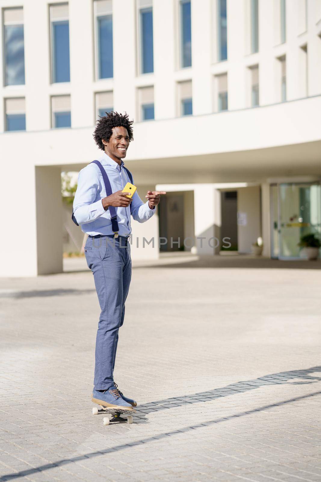 Black businessman on a skateboard holding a smartphone outdoors. by javiindy