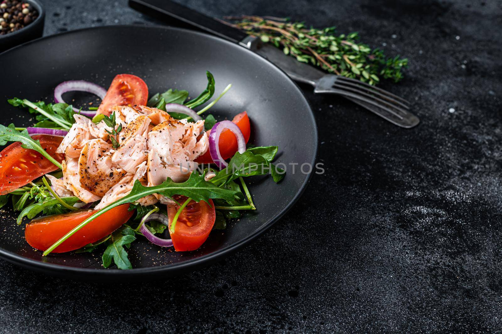 Salad with roasted salmon fillet steak, fresh salad arugula and tomato in a plate. Black background. Top view. Copy space by Composter