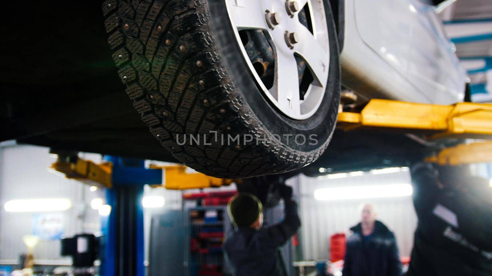 Car in auto service lifting for repairing, mechanics in garage, close up