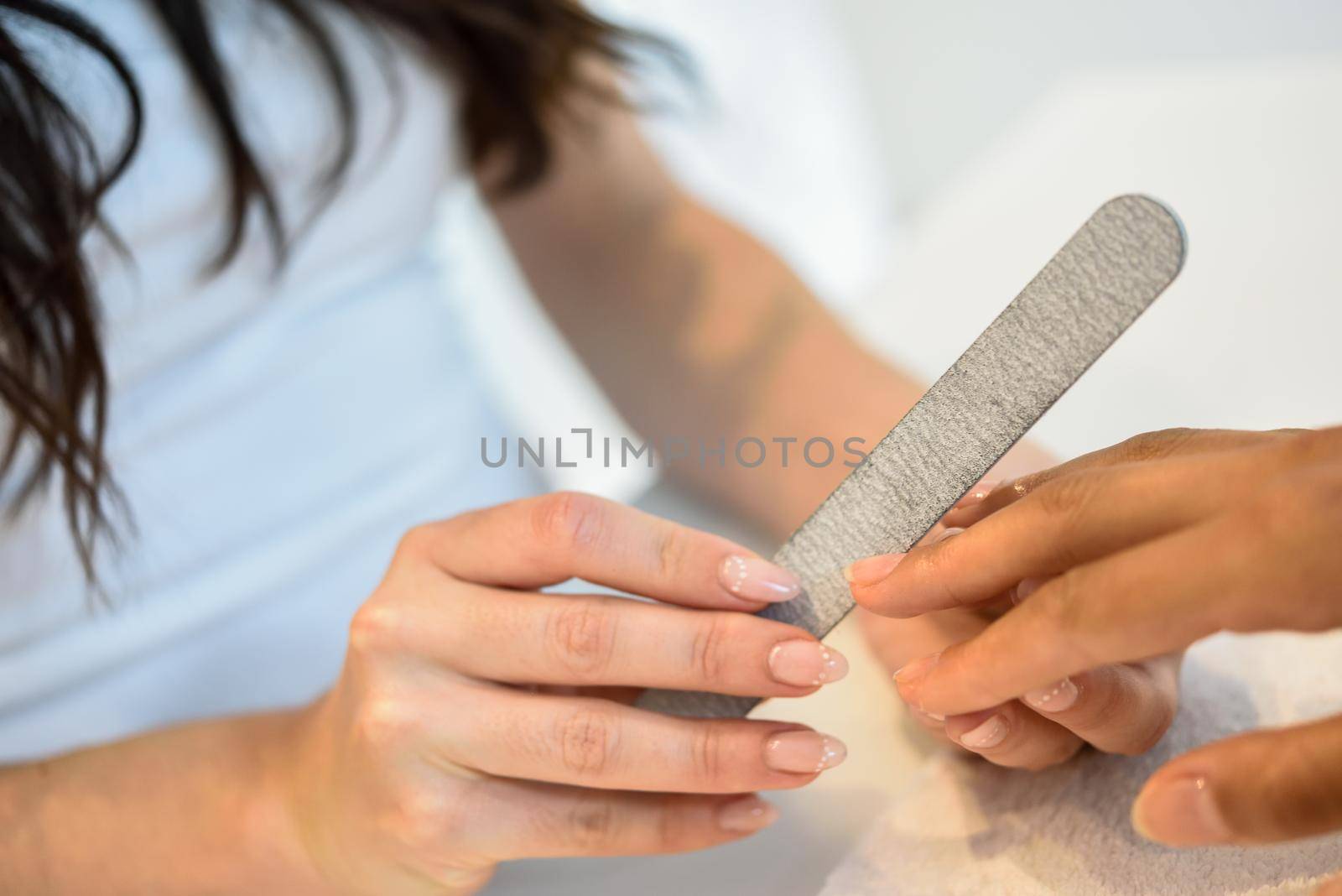 Woman in a nails salon receiving a manicure with nail file by javiindy