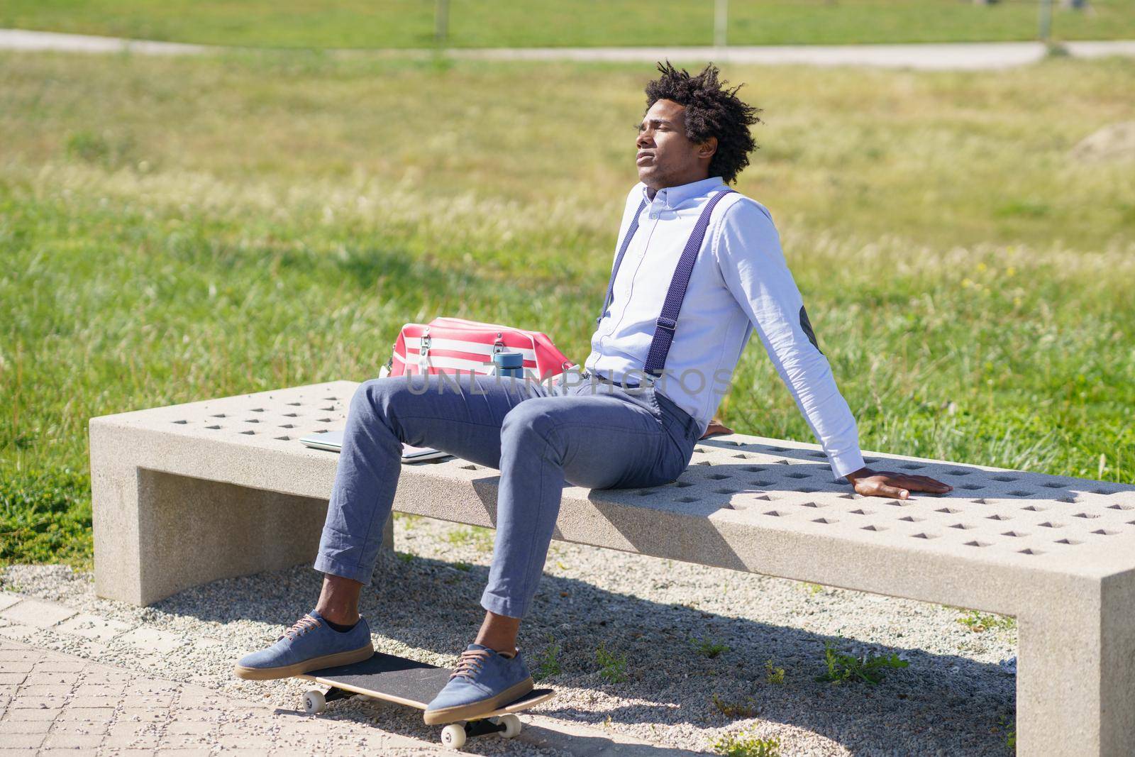 Black man with afro hair taking a coffee break sitting on a park bench. by javiindy