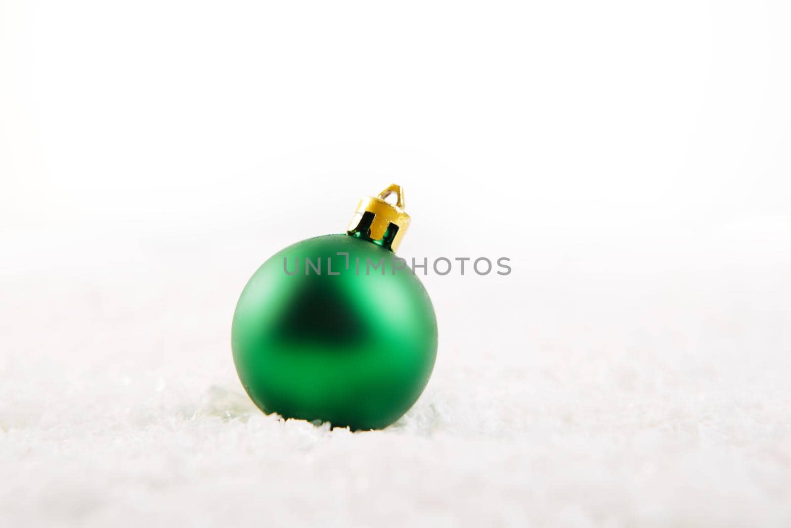 Green christmas ball on snow over white background .