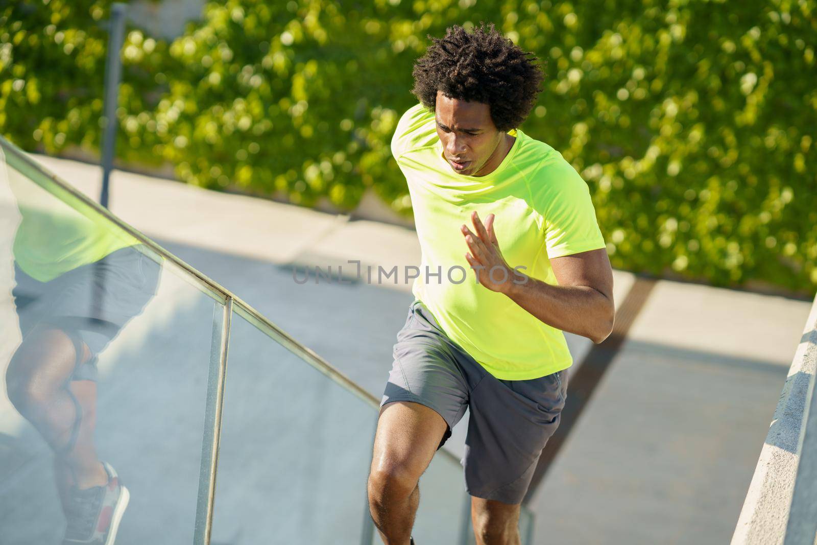 Black man running upstairs outdoors. Young male exercising in urban background.