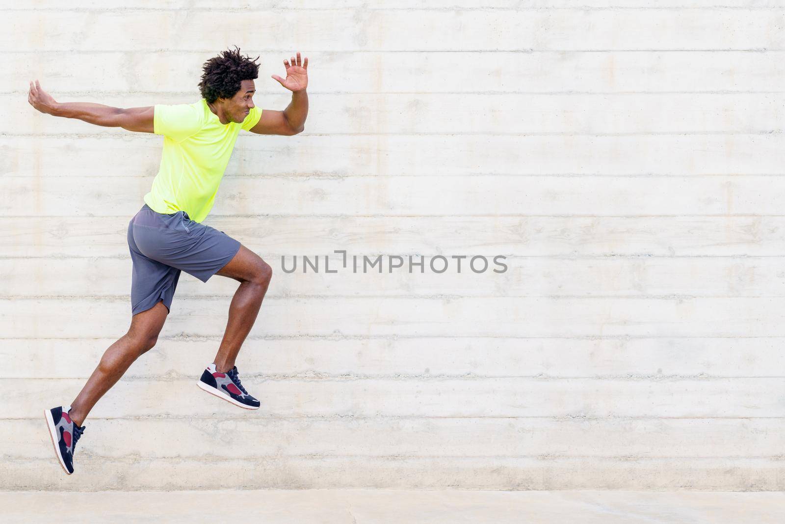 Black man training running jumps to strengthen his legs. Young male exercising in urban background.