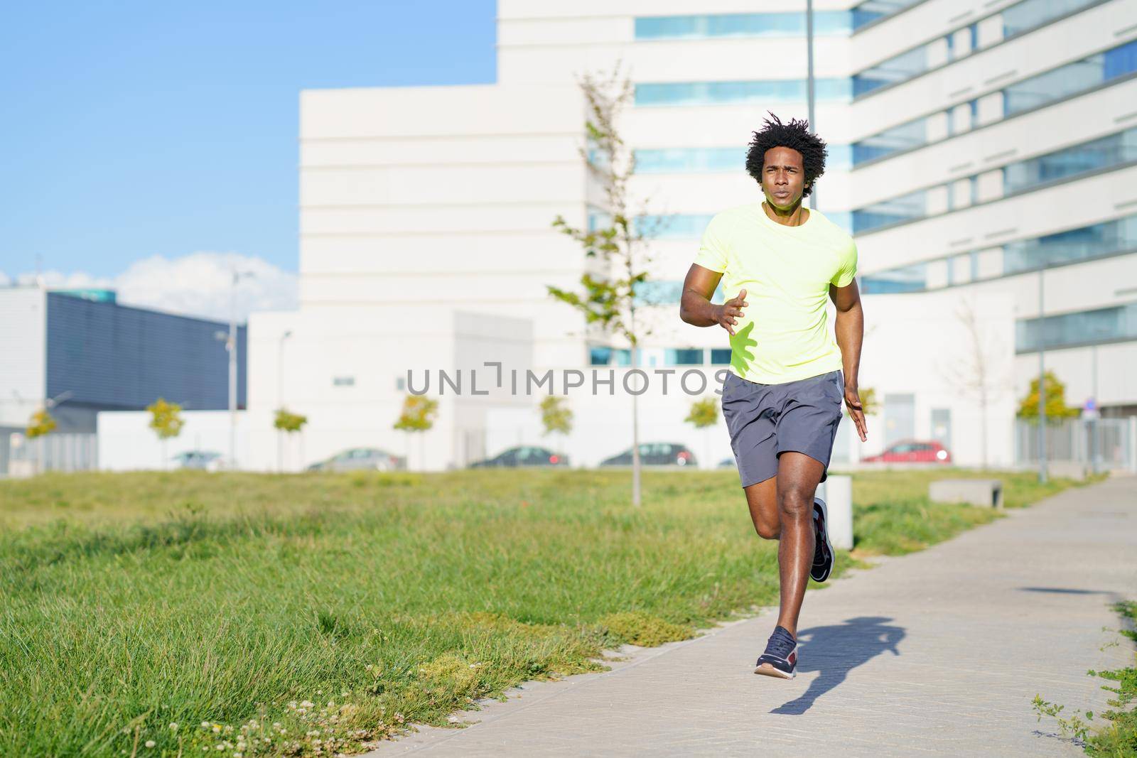 Black athletic man, afro hairstyle, running in an urban park. Young male exercising in urban background.
