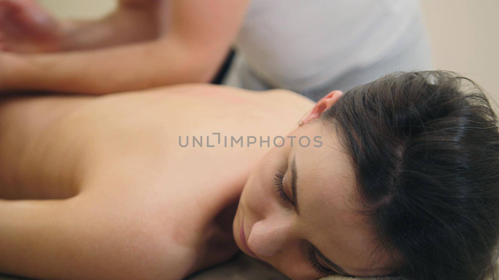 Young pretty half-nude female relaxing in spa salon - oil sesame massage table, close up