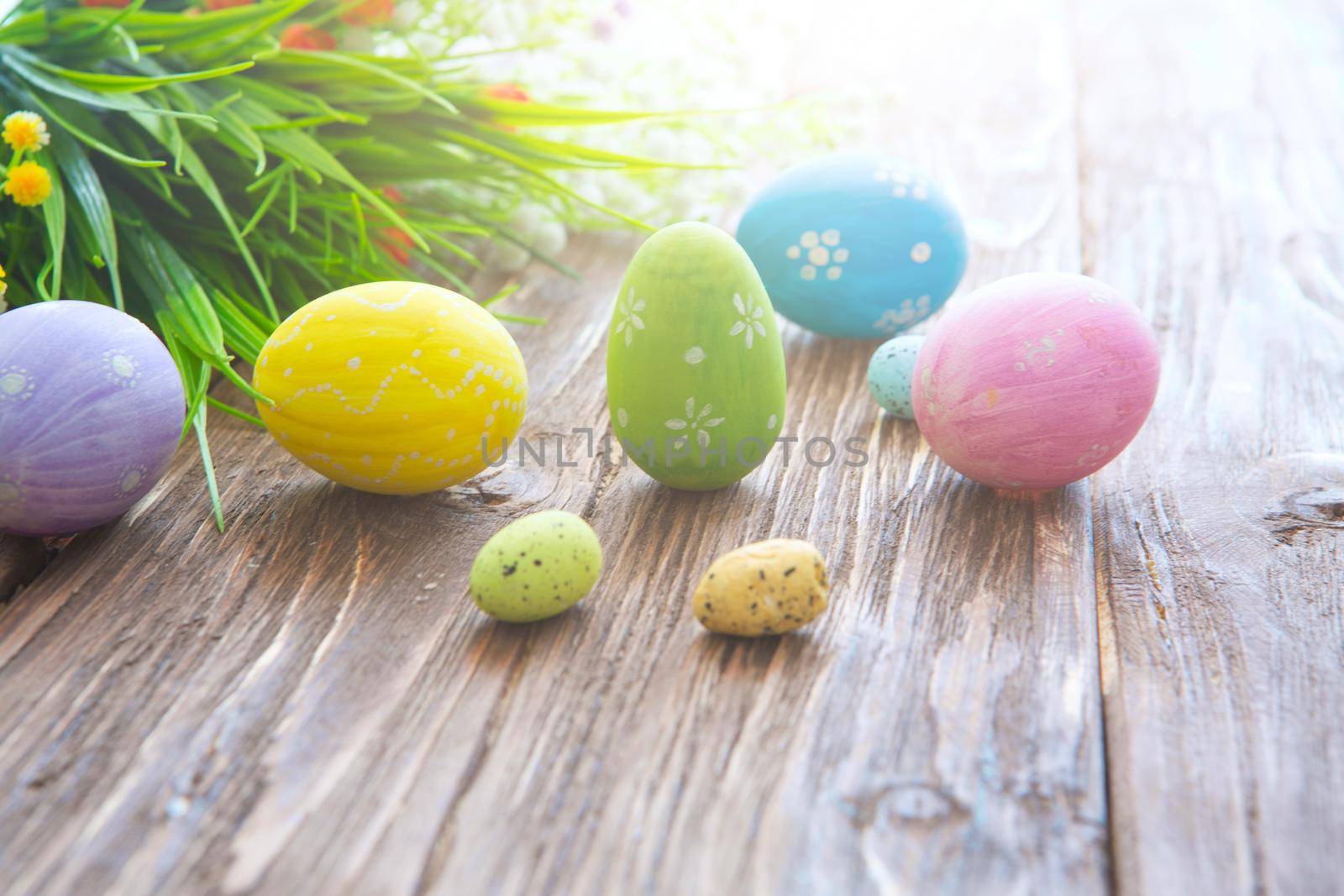 Colorful easter eggs and flowers on a rustic wooden planks .