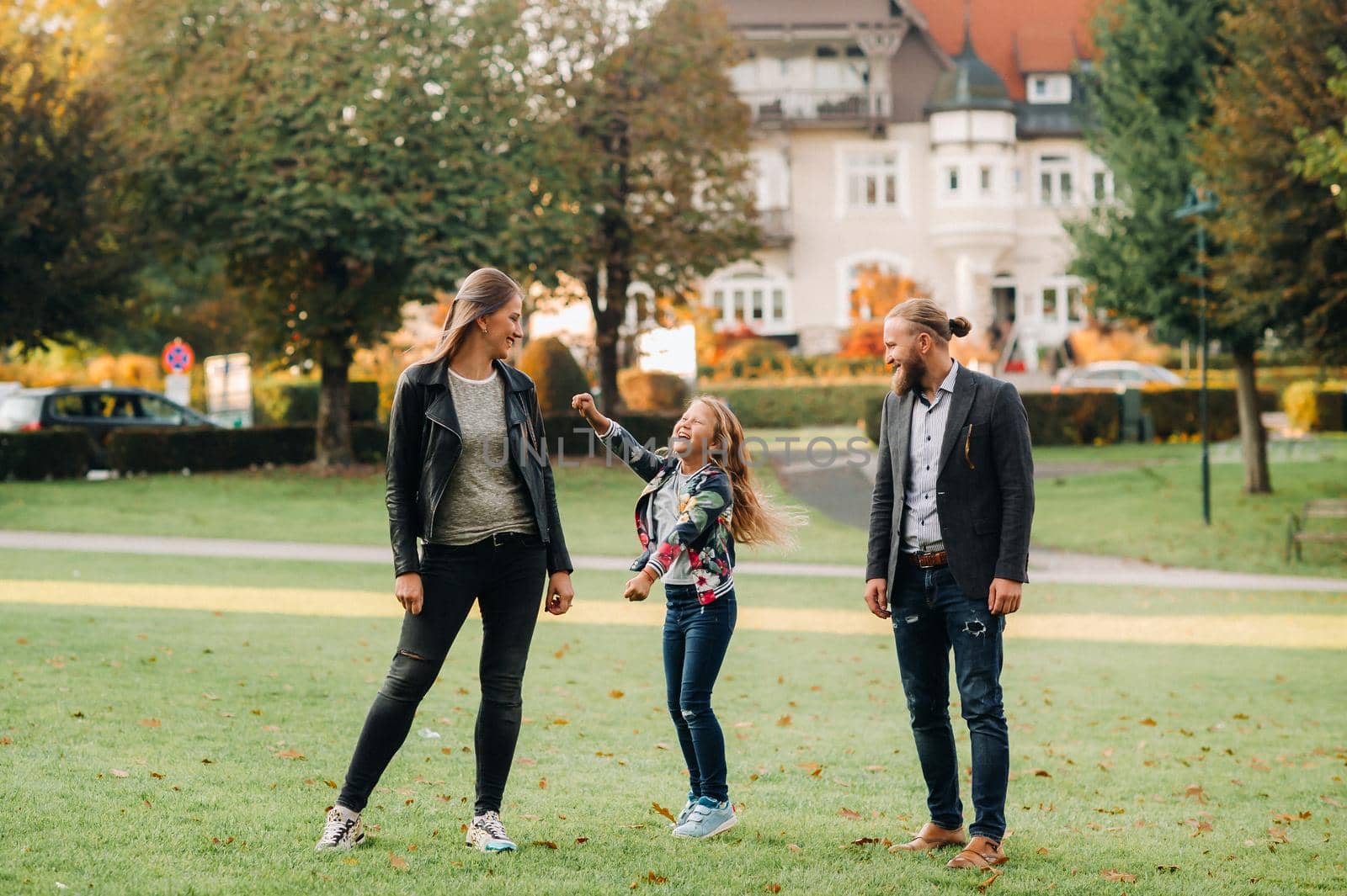 A happy family of three runs through the grass in Austria's old town.A family walks through a small town in Austria.Europe.Velden am werten Zee.