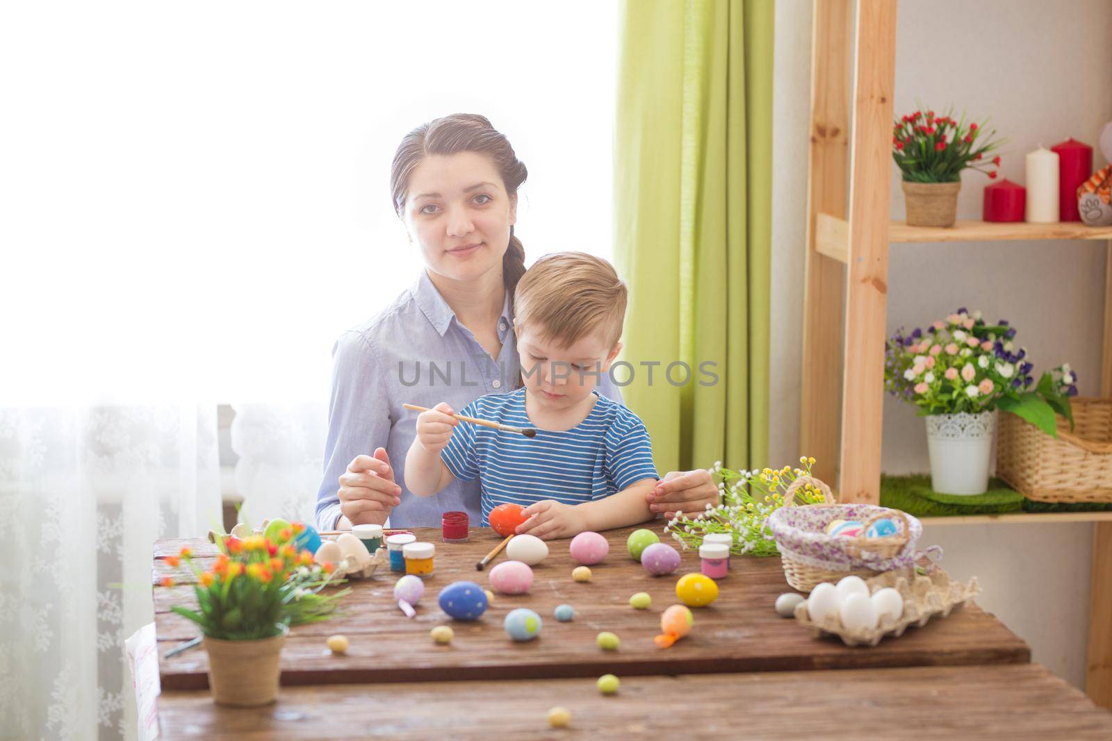 Easter concept. Happy mother and her cute child getting ready for Easter by painting the eggs.