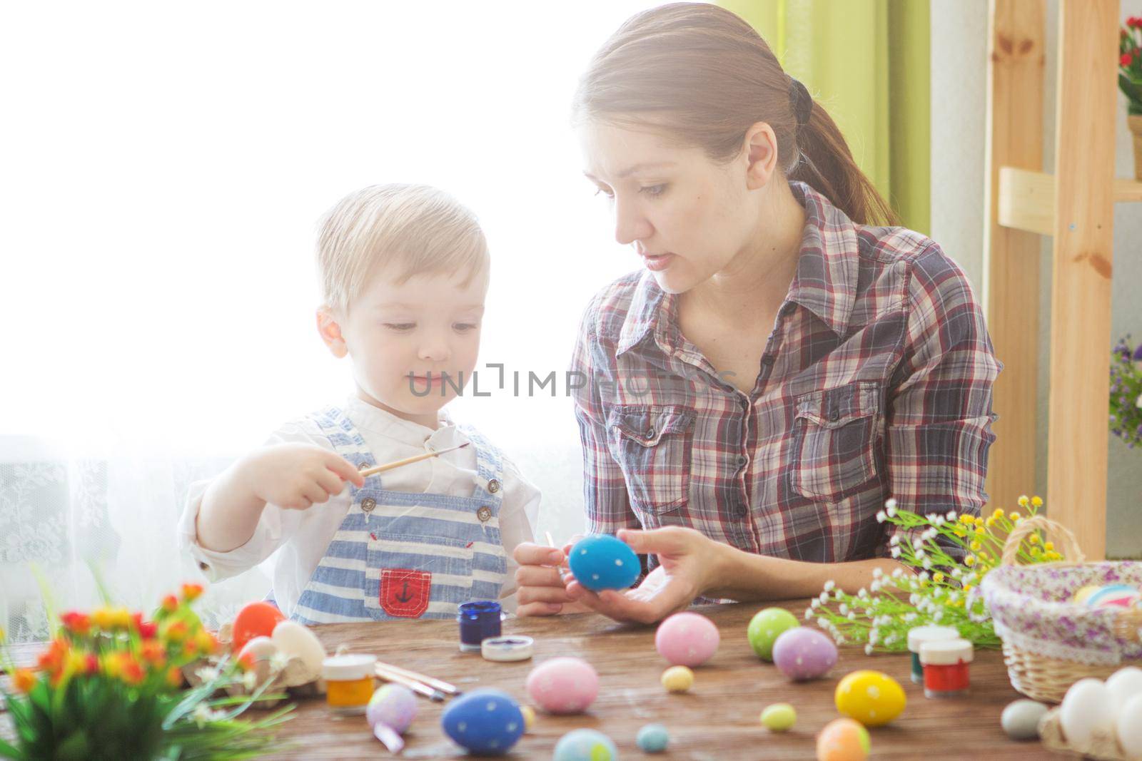 Easter concept. Happy mother and her cute child getting ready for Easter by painting the eggs.