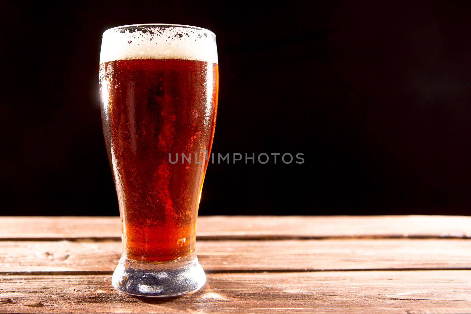 Glass of beer on wooden table on a black background