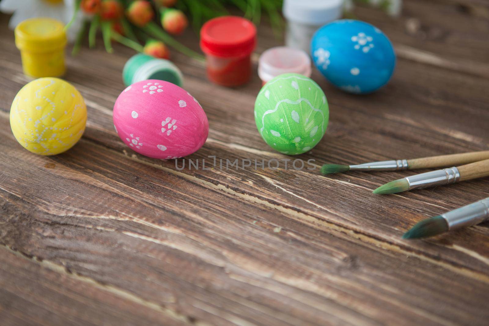 Colorful easter eggs, paint palette and brushes on a wooden table. Top view with copy space .