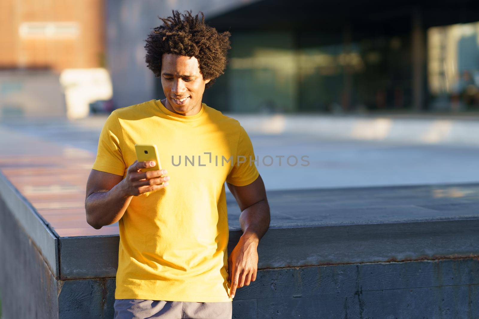 Black man with afro hair consulting his smartphone with some exercise app while resting from his workout.