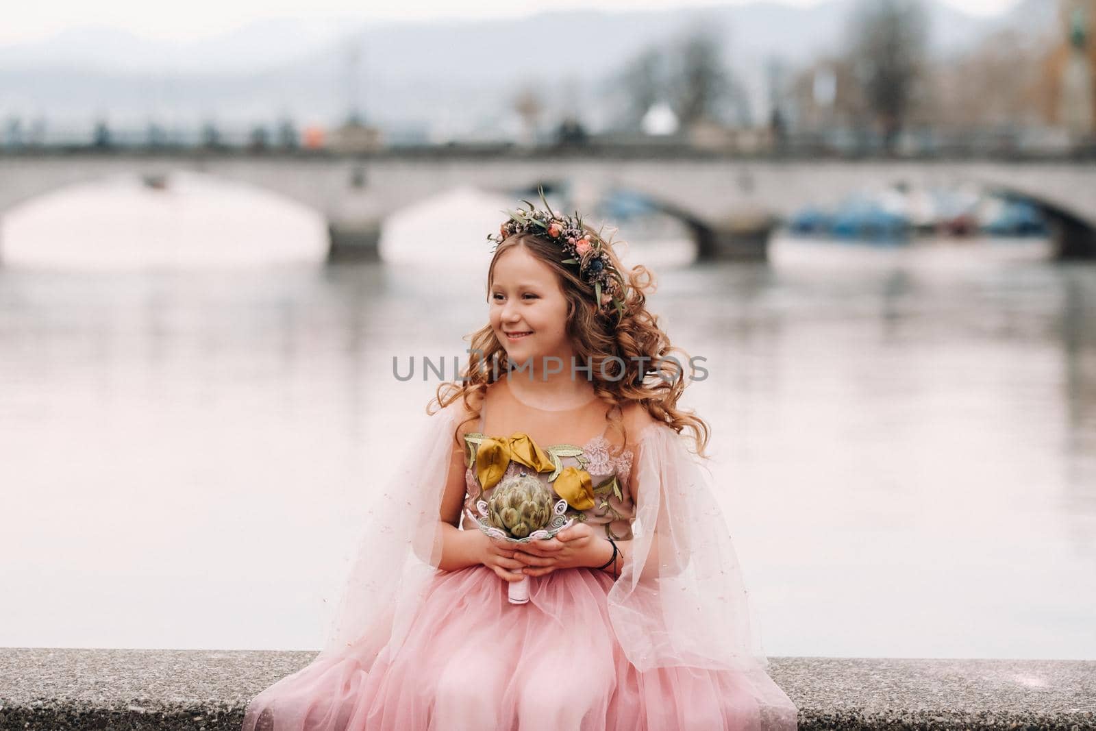 a little girl in a pink Princess dress with a bouquet in her hands walks through the old city of Zurich.Portrait of a girl in a pink dress on a city street in Switzerland.