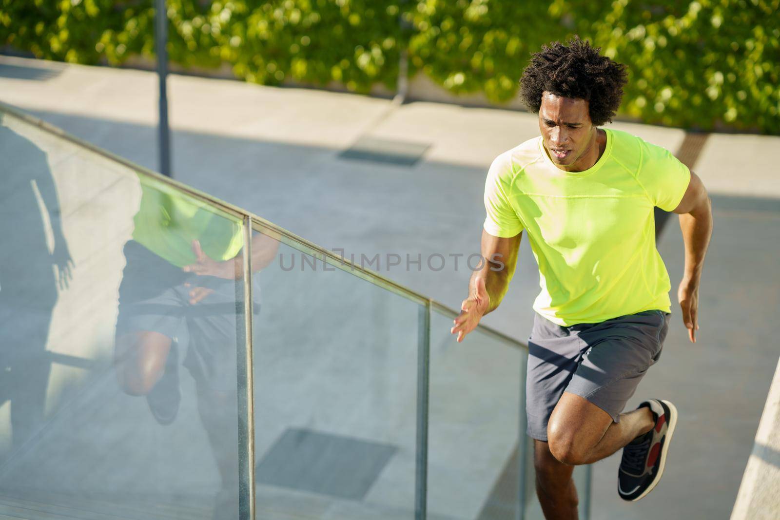 Black man running upstairs outdoors. Young male exercising. by javiindy