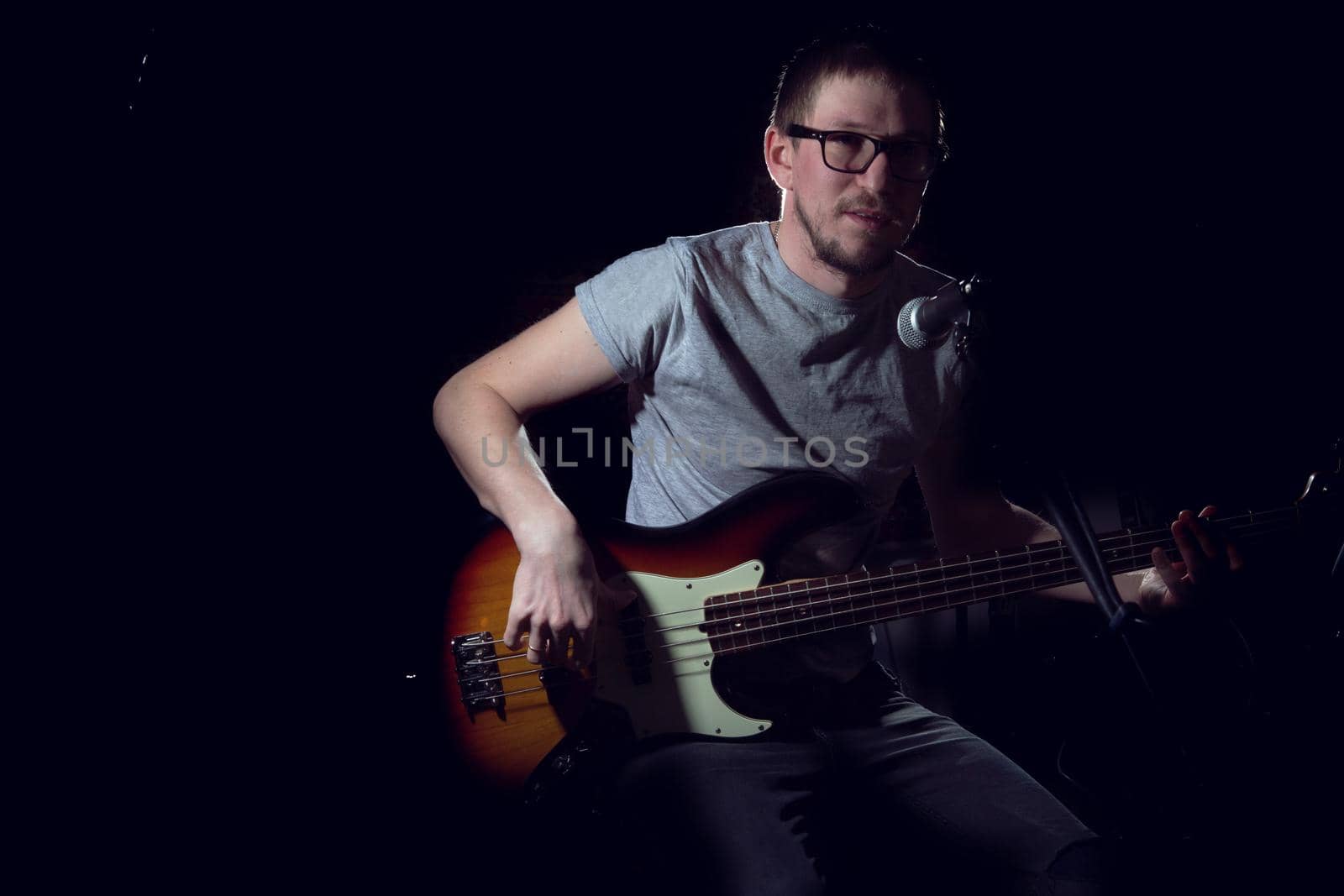 Man playing on electrical bass guitar on dark background