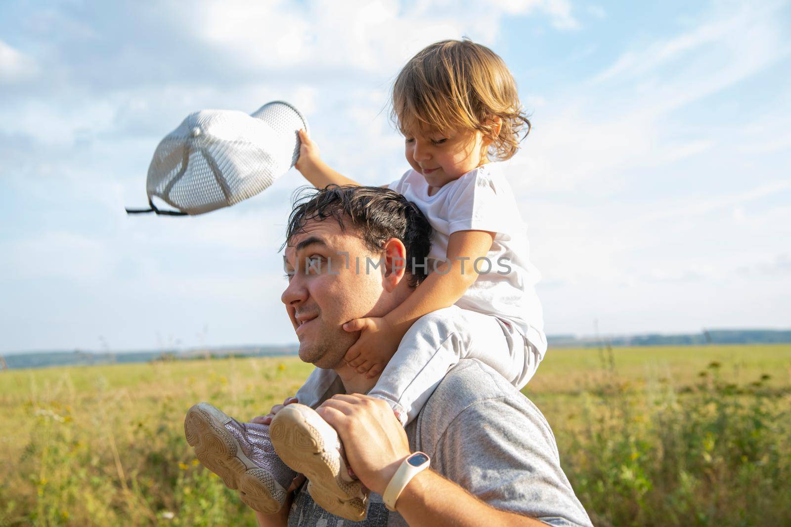 adorable toddler sits on dad's shoulders close-up. portrait of a child sitting on the father's neck by Mariaprovector