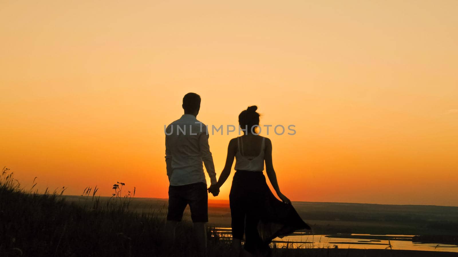 Young loving couple - brave man and beautiful girl at sunset silhouette, looking to sun, telephoto shot