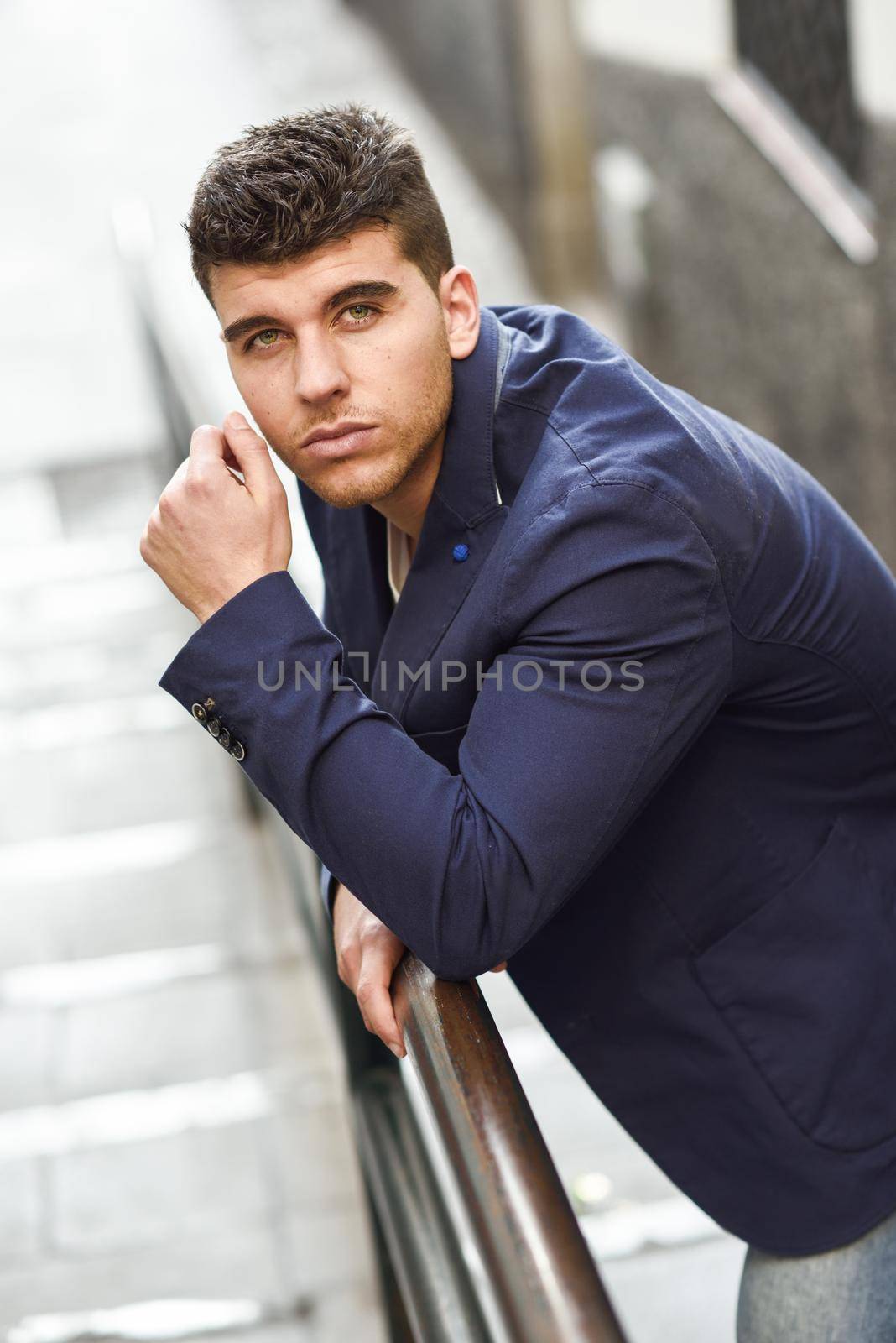 Good looking young man with blue eyes in the street. Model of fashion in urban background wearing white t-shirt, jeans and blue jacket