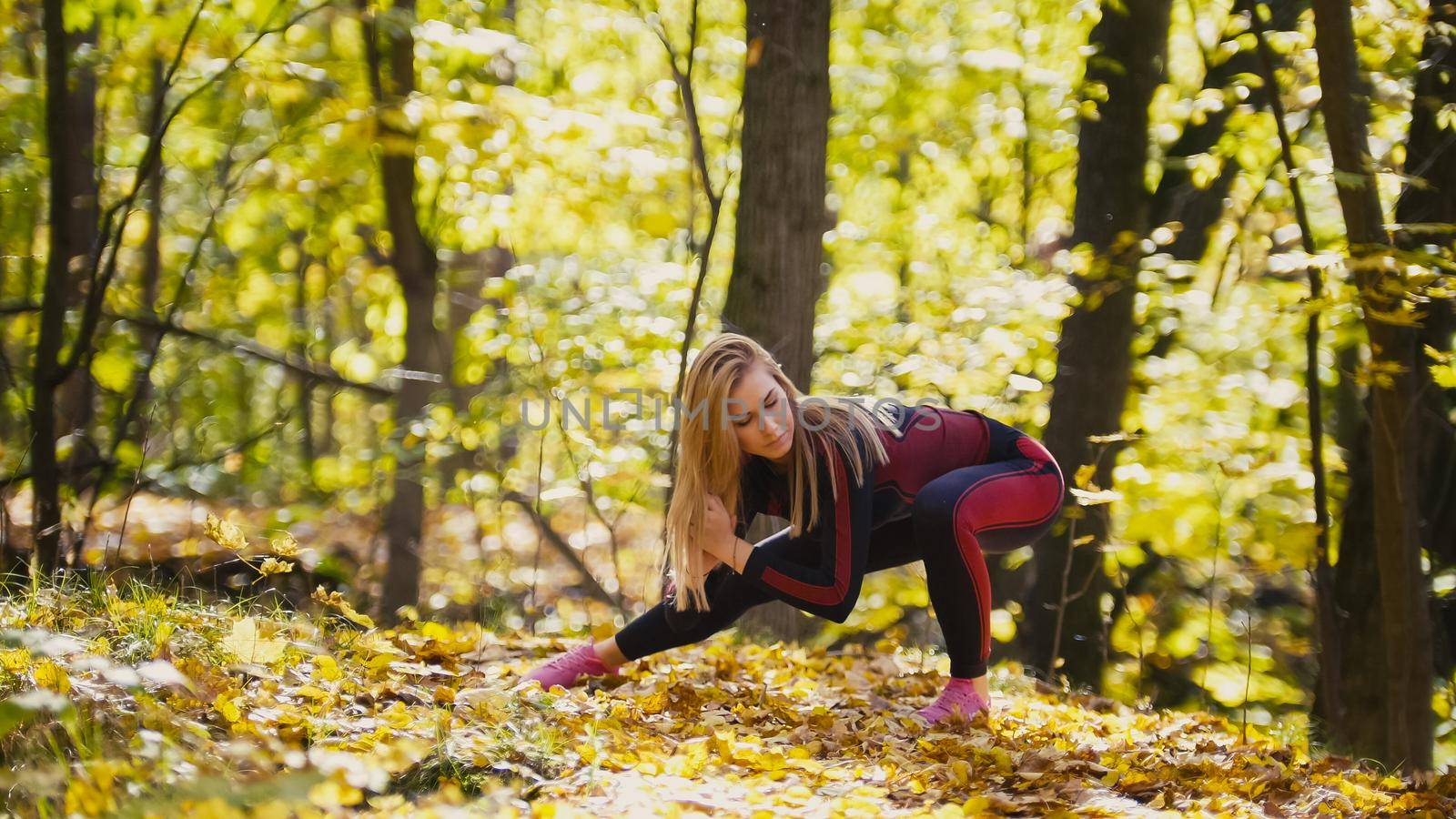 Woman doing fitness exercises outdoor. Female stretching in autumn forest. Slim girl at outdoor workout - squats, telephoto