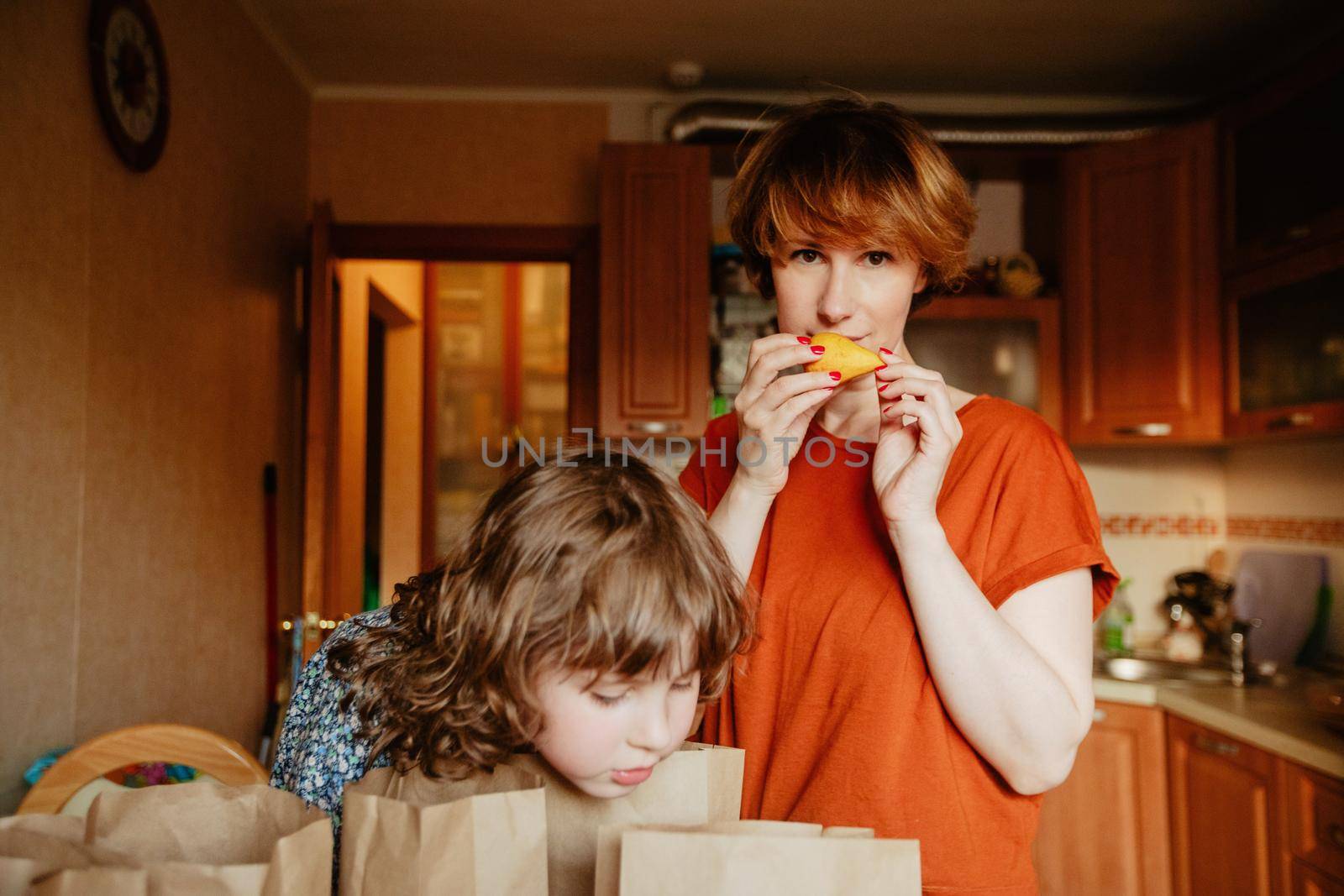 Woman and little girl standing together in kitchen with groceries in paper bags