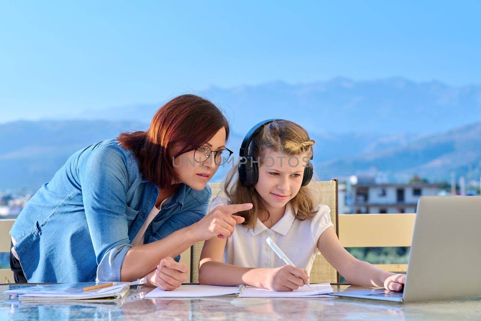 Child schoolgirl learning online with laptop, mom helping by VH-studio