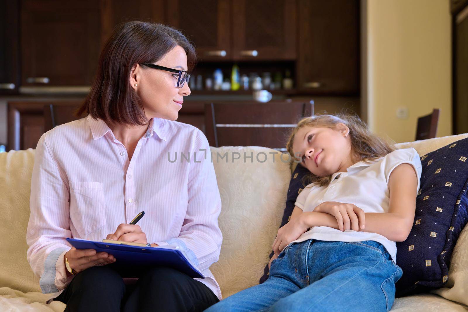 Smiling positive child girl and female psychologist teacher at session. Preteen student talking to counselor mentor therapist sitting on couch. Children mental health psychology childhood adolescence