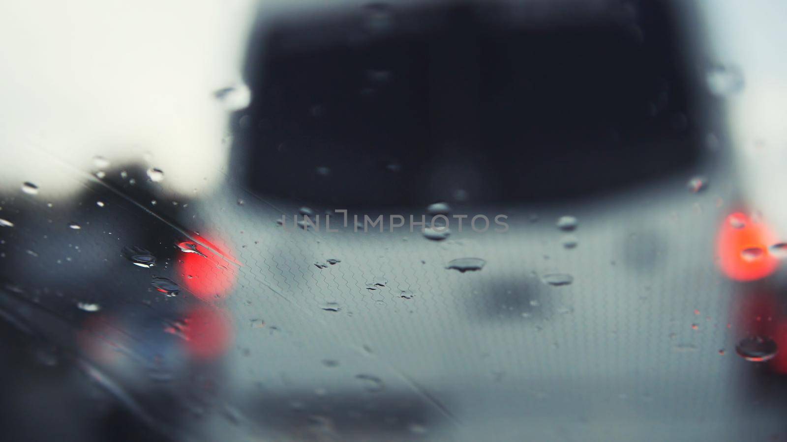 Car glass on a rainy day - defocused background. Moving waterdrops in the wipers of the windshield, close up, horizontal