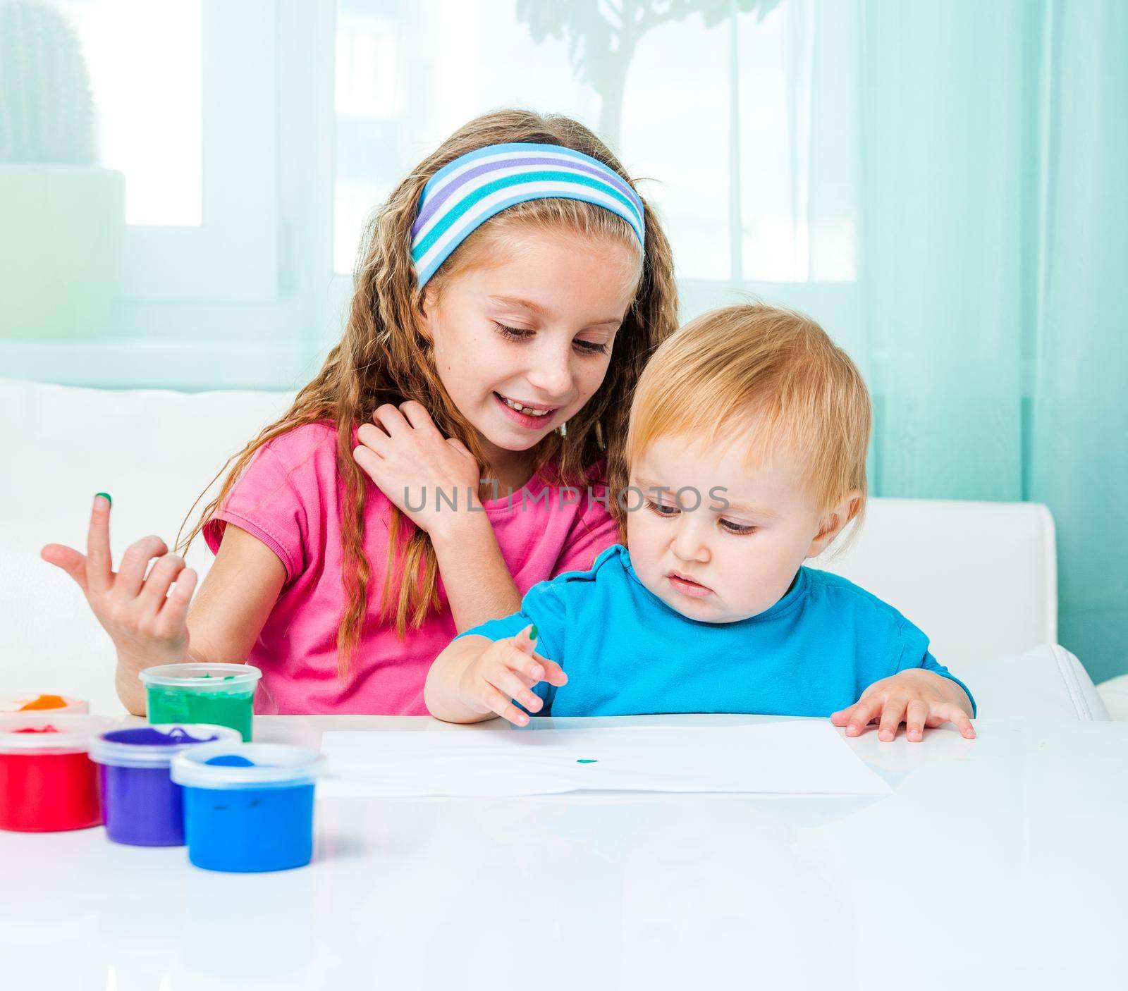 two happy sisters draw finger paints at home in bright living room