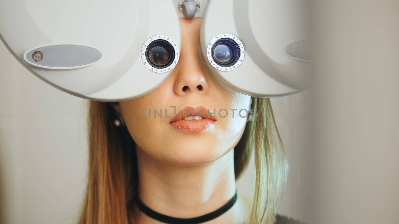 Attractive girl with red lips checks the eyes on the modern equipment in the medical center, telephoto, horizontal