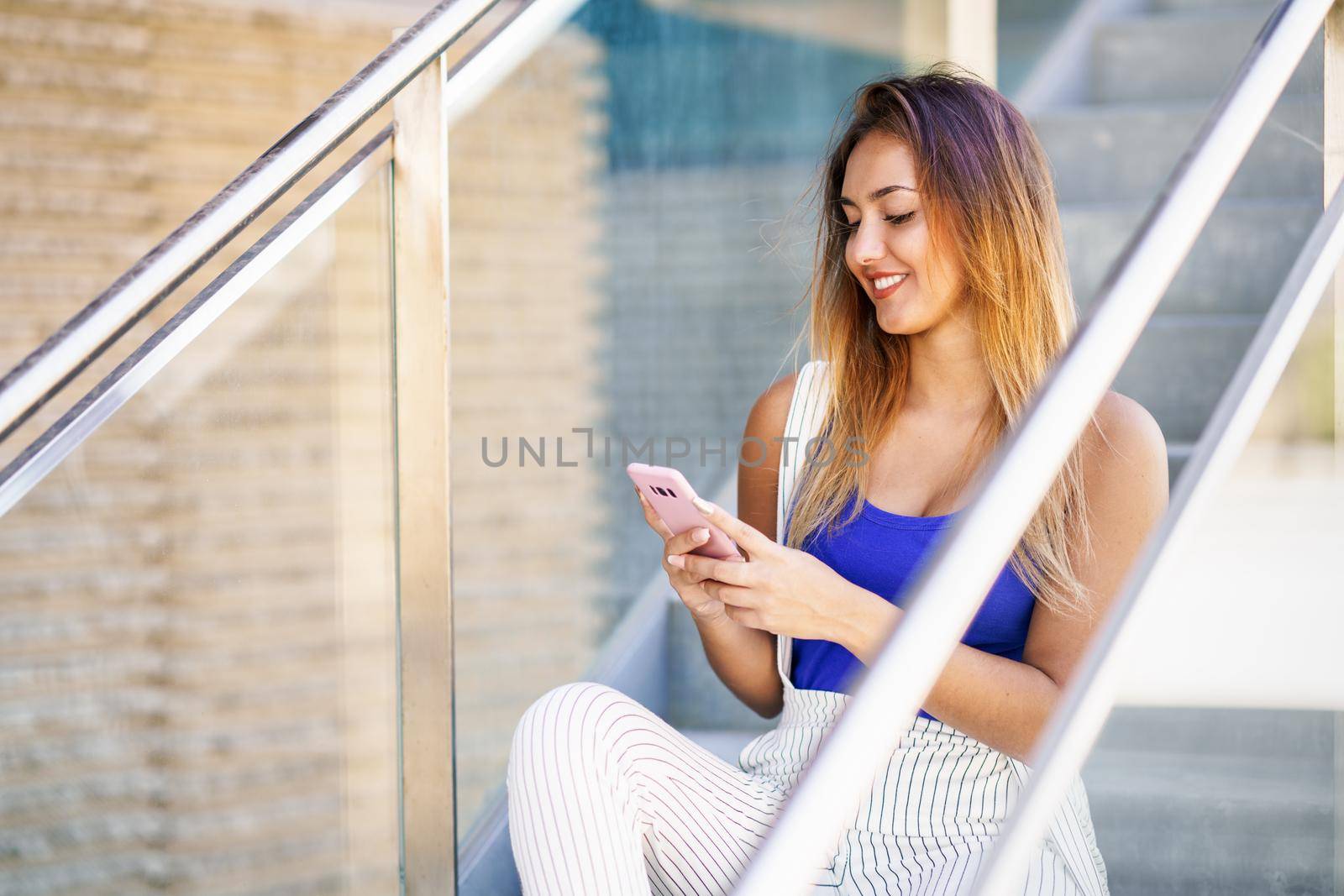 Young woman using a touchscreen smartphone wearing casual clothes. Girl sitting outdoors with gel nails.