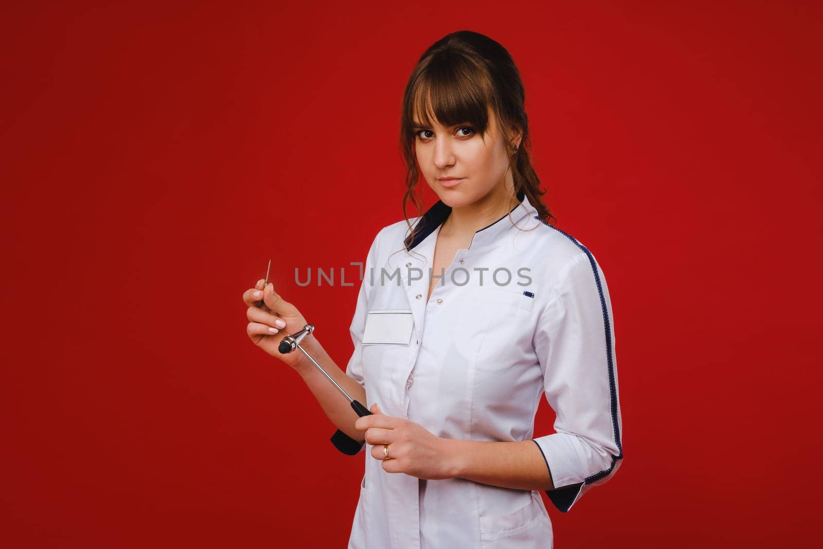 a beautiful doctor girl holds a reflex hammer and smiles at the camera isolated on a Red background.