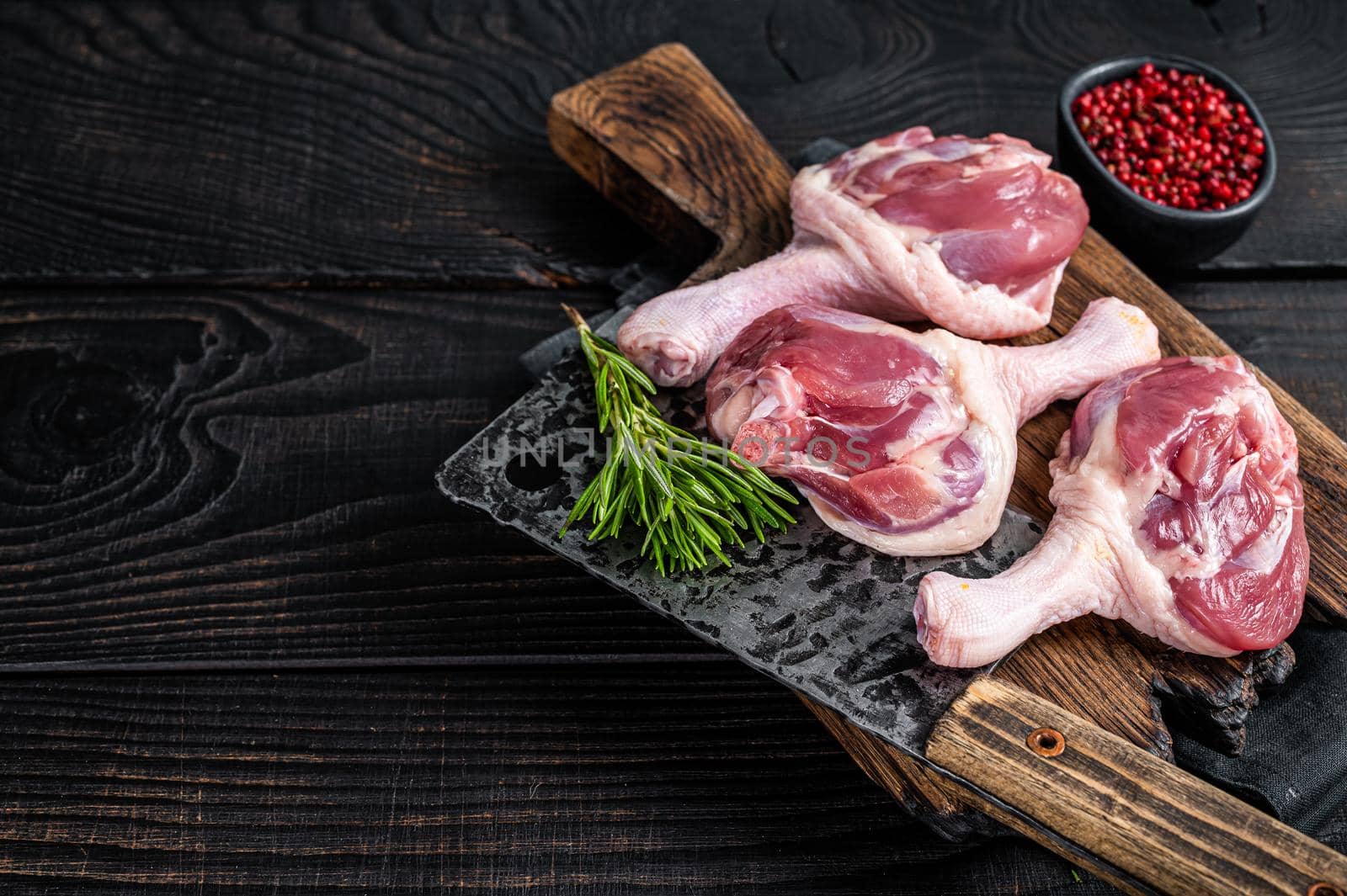 Raw Duck thighs on butcher board with meat cleaver. Black wooden background. Top view. Copy space.