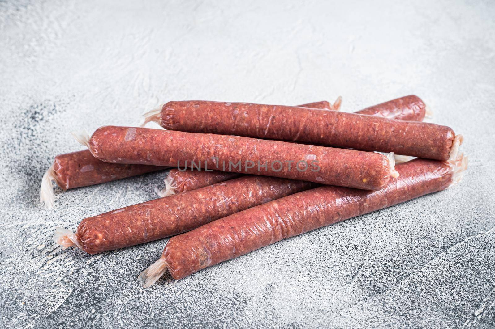 Raw butchers sausages in skins with herbs on kitchen table. White background. Top view by Composter