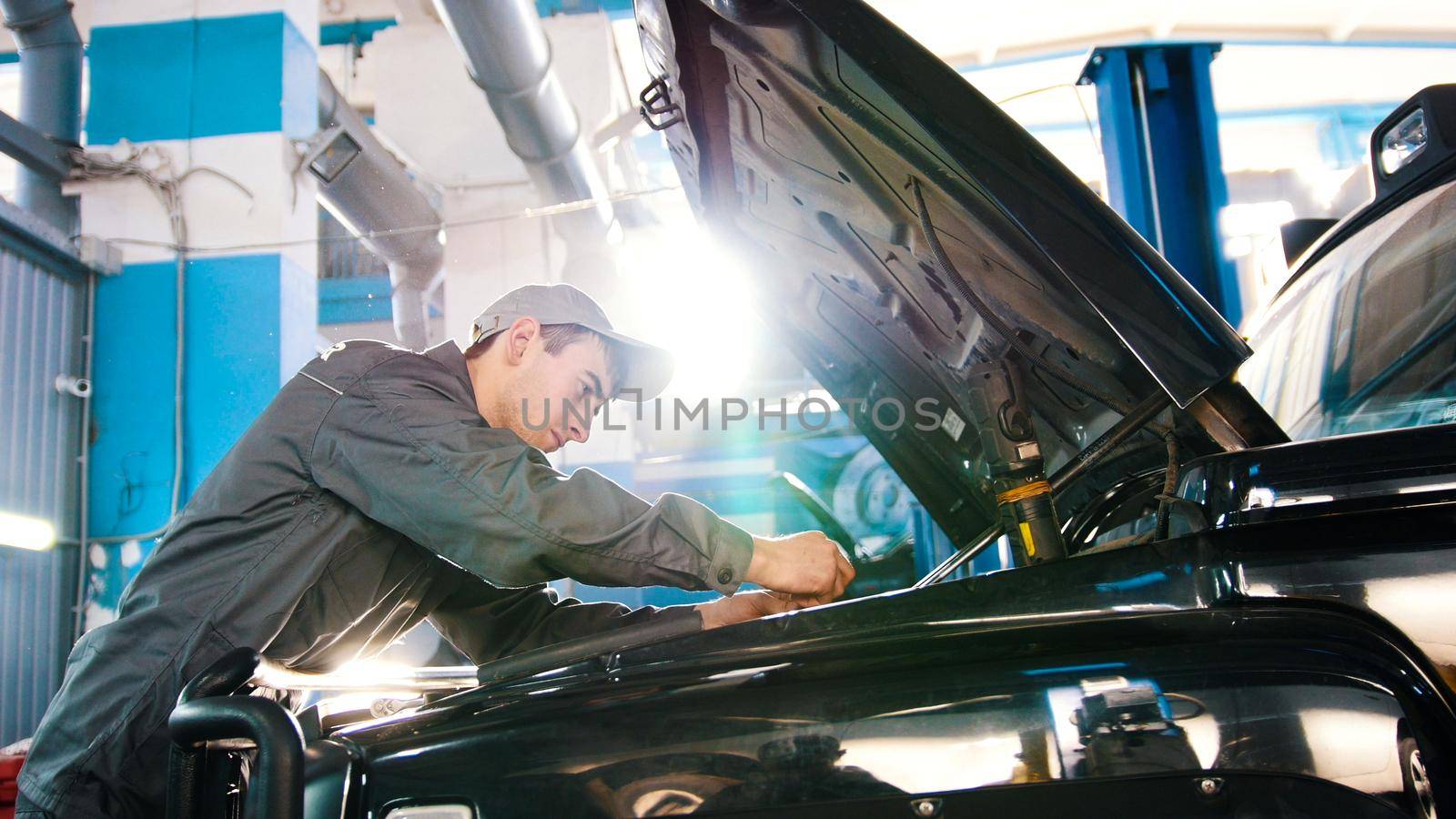 Mechanic in car service - repairing in engine compartment for luxury SUV by Studia72