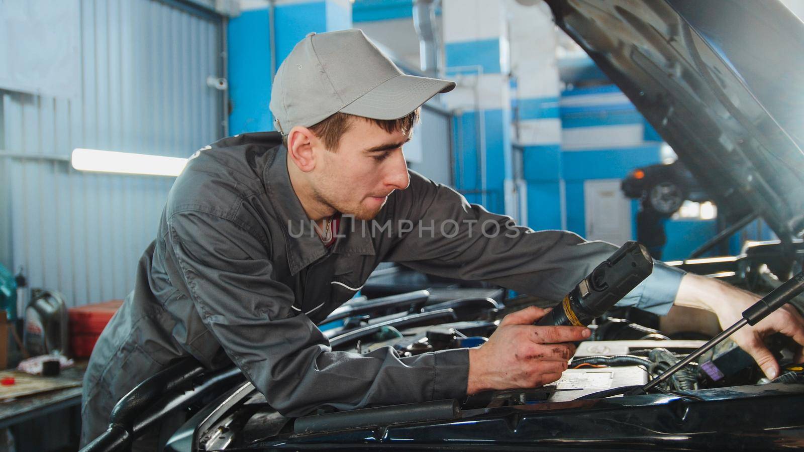 Mechanic in overalls looking to hood of the car - automobile service repairing, close up
