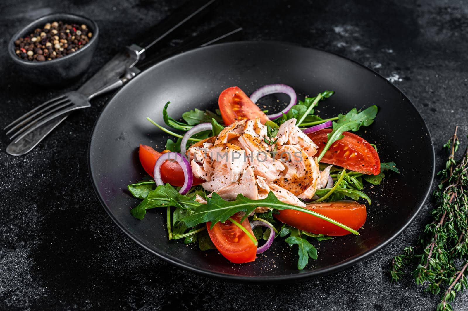 Salad with baked salmon fillet steak, fresh arugula and tomato in a plate. Black background. Top view by Composter