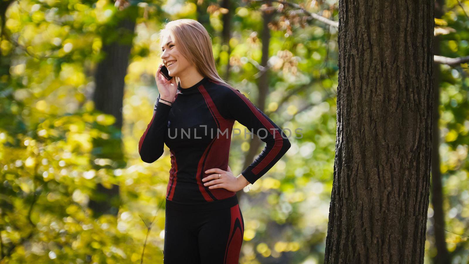 Young, sporty woman talking on cellphone and smiling at autumn park outdoor, close uptelephoto