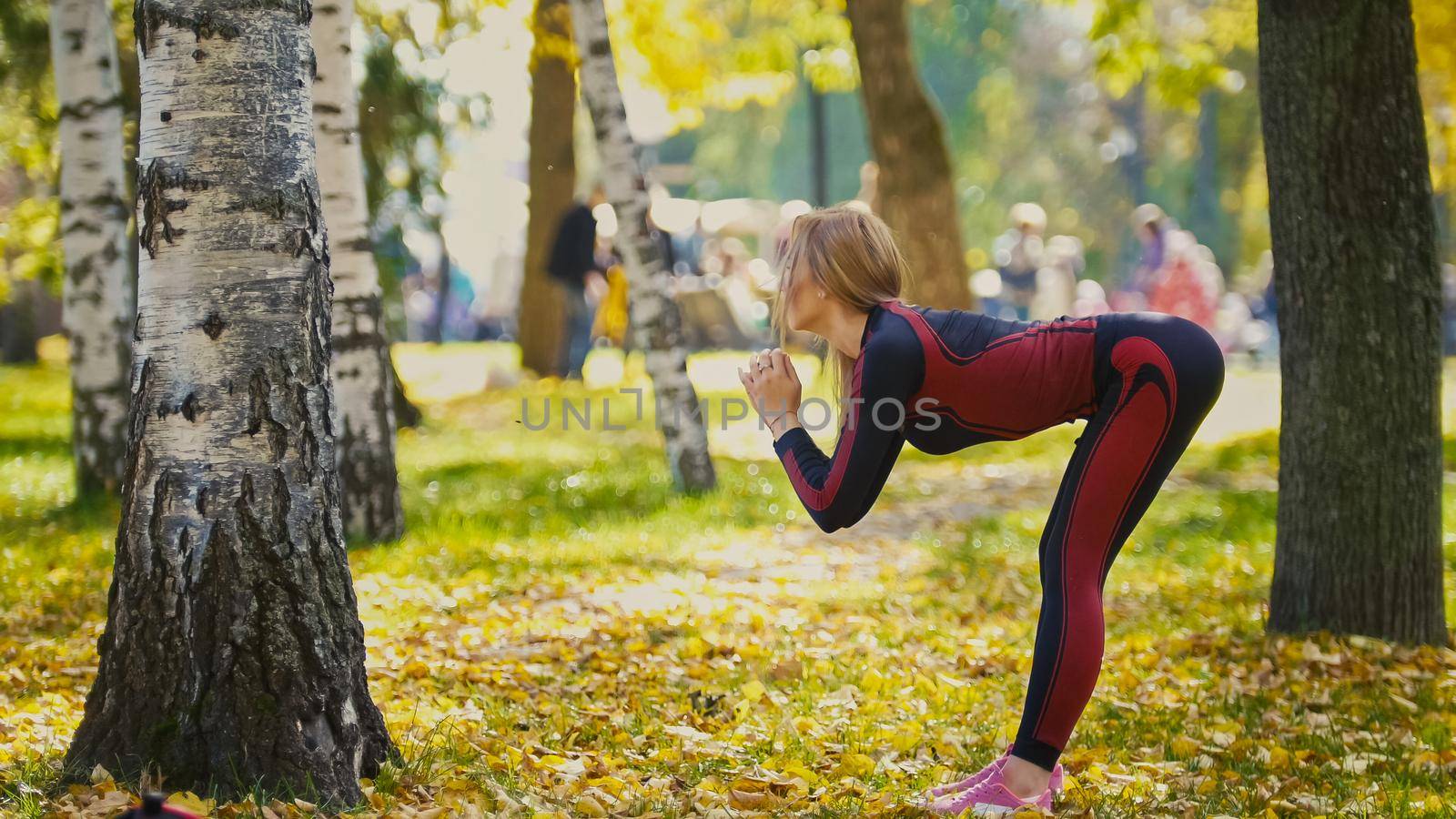 Sexy Attractive female blonde bikini-fitness model stretching in the autumn park on ground covered yellow leaves - the tilt of the body, telephoto