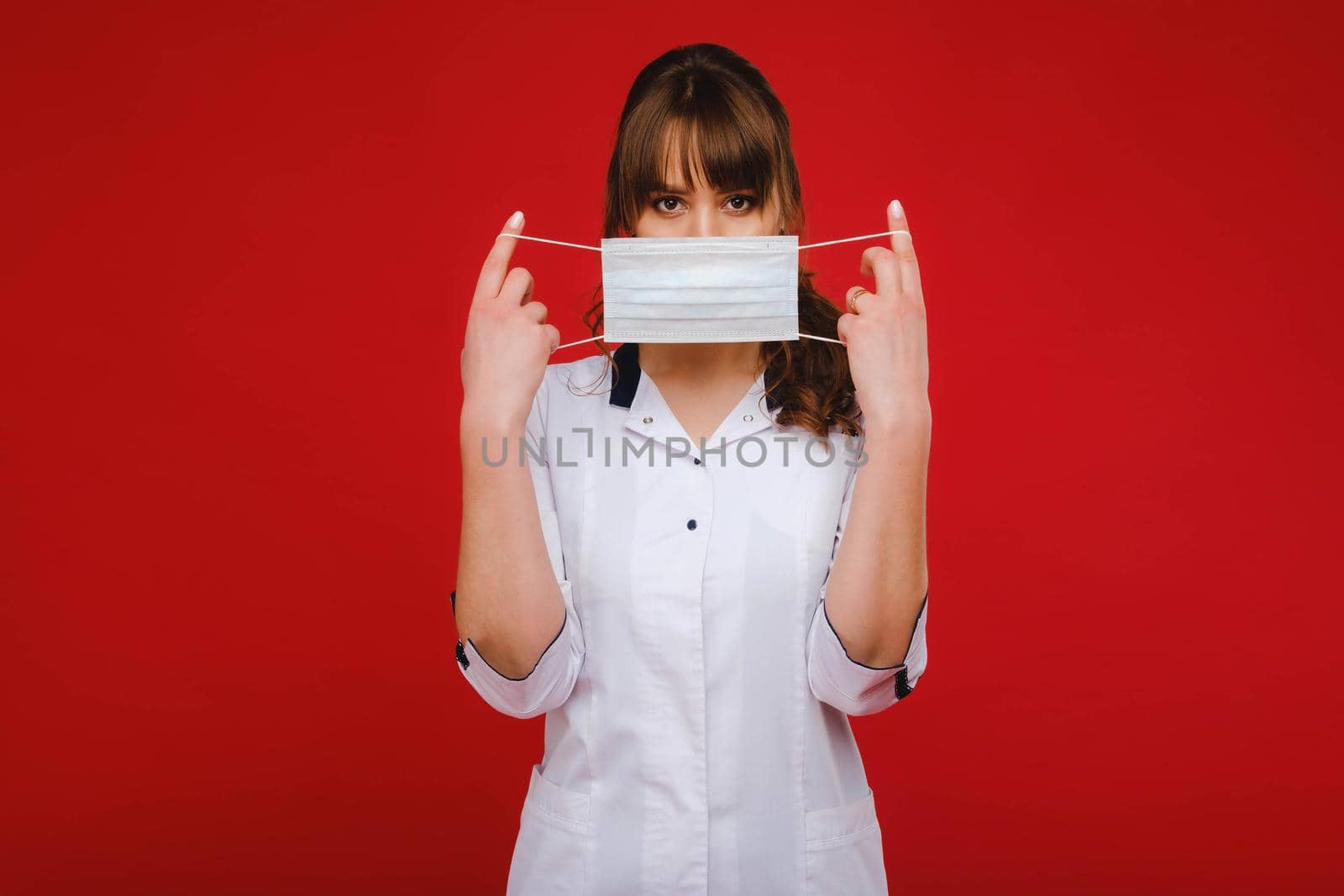 A female doctor stands in a medical mask isolated on a red background