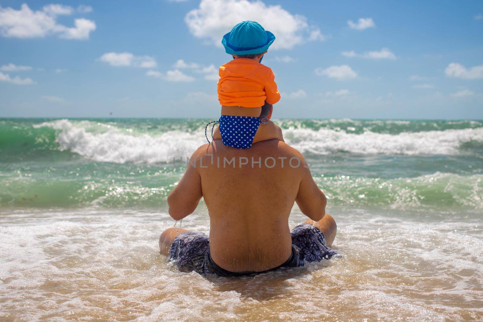 family values concept. Dad defender. the baby sits on dad shoulders, dad sits on the beach and a wave comes.
